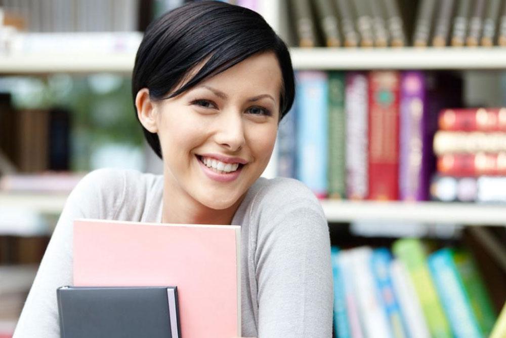 Smiling young lady with books in background at office