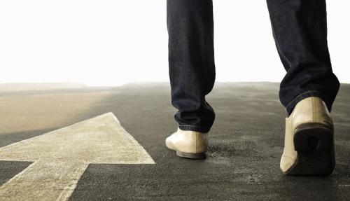 Closeup of person walking along a road with conceptual arrow leading forward