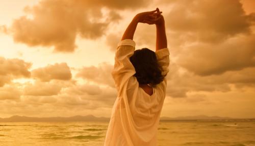 Lady stretching arms on beach at sunset