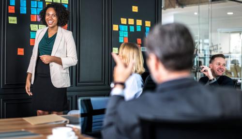 Black middle aged lady in front of screen presenting to senior leaders